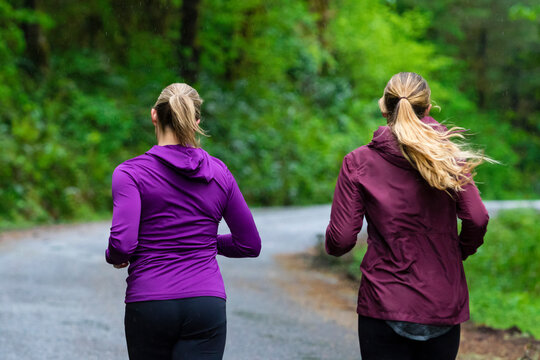 Rear view of two female joggers running on road in rain, Oregon, USA