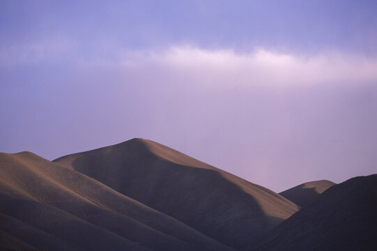 Clouds are colored by sunset light over bare hills, Bamiyan