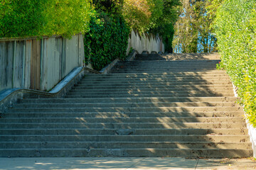 Sprawling staircase in a park or public area for access through suburban neighborhood with cement stairs in shade