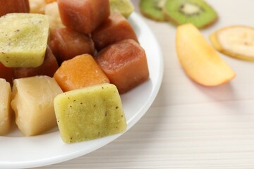 Different frozen fruit puree cubes and ingredients on white wooden table, closeup