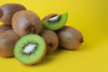 Heap of whole and cut fresh kiwis on yellow background, closeup. Space for text
