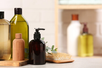 Shampoo bottles, hair brush and leaves on light grey table, space for text