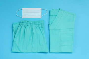 Medical uniform and protective mask on light blue background, flat lay
