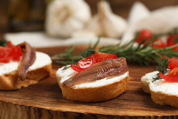Delicious sandwiches with cream cheese, anchovies and tomatoes on wooden board, closeup