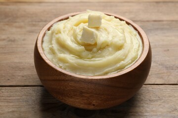 Bowl of delicious mashed potato with butter on wooden table, closeup