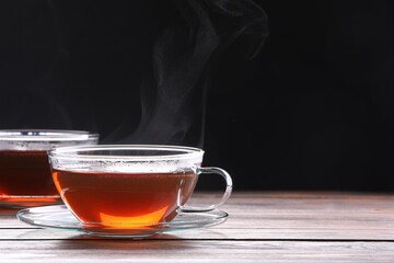 Glass cups with tea on wooden table against black background, space for text