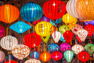 Fototapeta na wymiar Close up of a collection of glowing Asian lanterns of various colours hanging in a shop at Hoi An in Vietnam