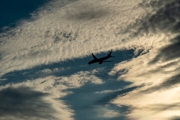 Fototapeta na wymiar Jet plane small silhouette arrive from travel, sunset evening clouds. Big passenger airplane crossing the sky.
