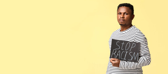 African-American man holding poster with text STOP RACISM on yellow background with space for text