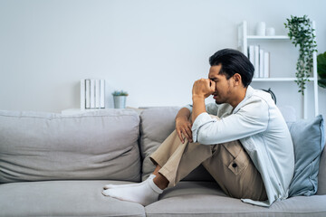 Fototapeta premium Asian young upset depressed man sitting alone in living room at home. 