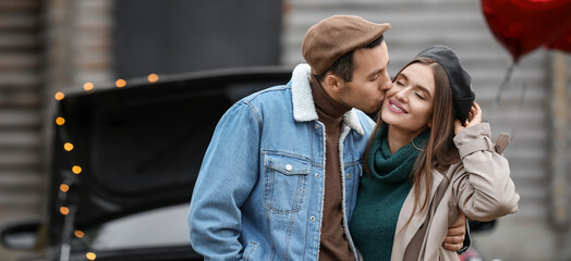 Happy young man kissing his girlfriend near car outdoors. Valentine's Day celebration