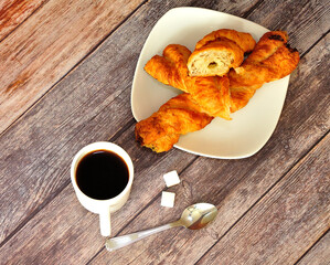 A cup of hot black coffee, two sugar cubes and a plate with two spiral puff pastries on a wooden table.