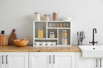 Jars with cereals, spices and utensils on kitchen counter