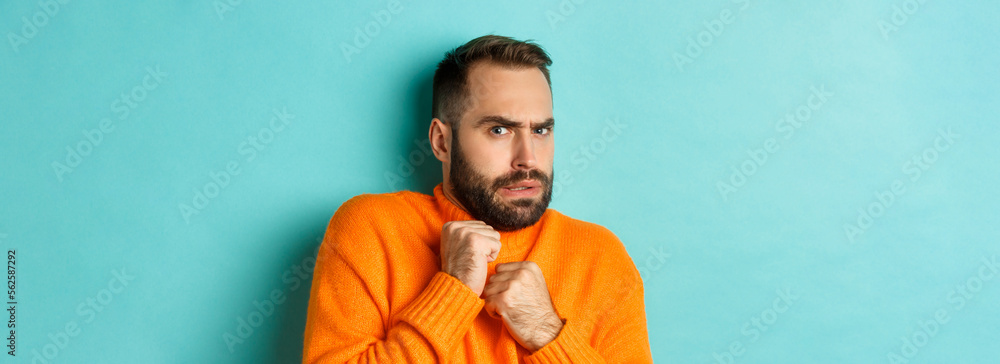 Wall mural Close-up of scared bearded man looking startled and displeased, jumping from fear, standing over light blue background