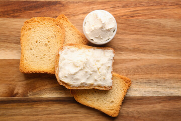 Toasts with tasty cream cheese on wooden background