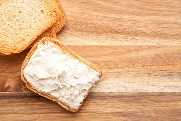 Toasts with tasty cream cheese on wooden background