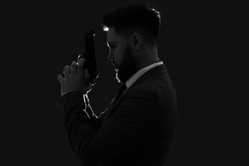 Silhouette of young man in suit with gun on dark background