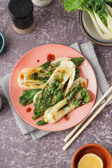 Plate of tasty stewed pak choi cabbage with soy sauce on grunge background