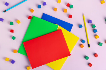 Composition with colorful notebooks, pencils and cubes on pink background