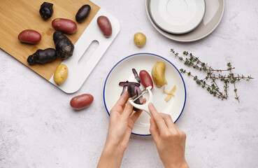Woman peeling different types of potatoes on grunge table