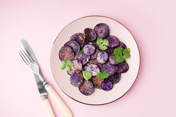 Plate with slices of fried purple potatoes and cilantro on color background