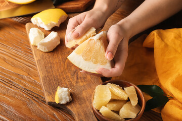 Female hands with piece of fresh pomelo fruit on wooden background