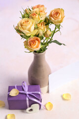 Vase with beautiful rose flowers, gift box and blank card on table near color wall