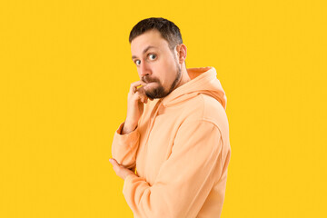 Handsome man in hoodie biting nails on yellow background