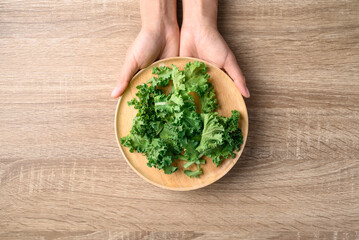 Green Kale or leaf cabbage on wooden plate with hand, Healthy vegetable, Table top view
