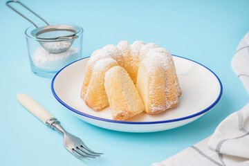 Plate with delicious cake, fork and glass of powdered sugar on blue background