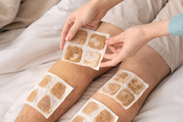 Woman putting mustard plaster onto ill man's leg in bedroom, closeup