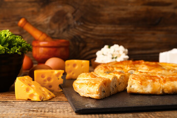 Slate board with delicious cheese pie and ingredients on wooden background