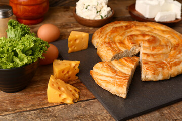 Slate board with delicious cheese pie and ingredients on wooden background
