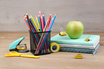 Pencils holder, notebooks with green apple, stapler and scissors on wooden background