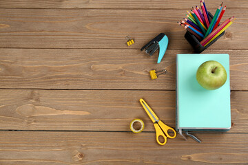 Fototapeta na wymiar Pencils holder, notebooks with green apple, stapler and scissors on wooden background