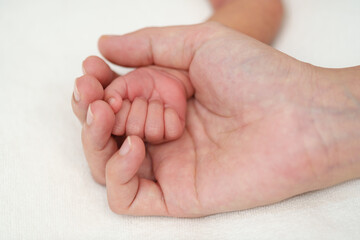mother holding newborn baby hand on bed