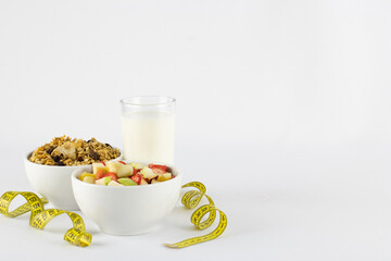 Chopped tropical and juicy fruits, granola and milk cup, wrapped in measuring tape, symbolizing healthy life, on white background