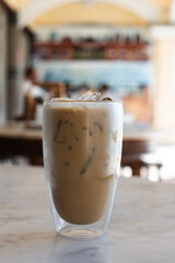 Iced coffee in a clear glass on a white marble table The back is a shelf. Equipment for tea and coffee blurred vision