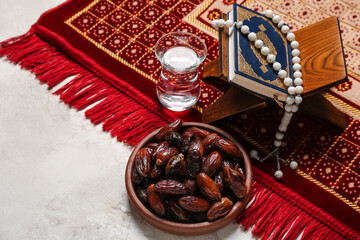 Dried dates, glass of water, Koran, prayer beads and mat for Ramadan on light background