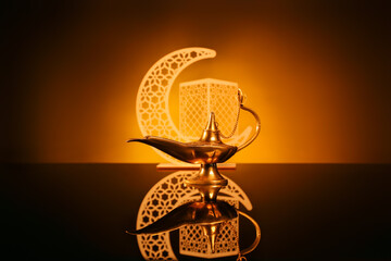 Aladdin lamp of wishes and decorative crescent for Ramadan on table against dark yellow background