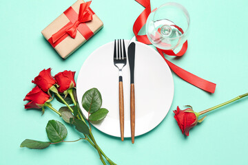 Table setting with rose flowers, glass and gift on turquoise background. Valentine's Day celebration