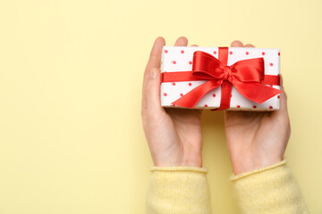 Woman holding gift box with beautiful bow on yellow background. Valentine's Day celebration