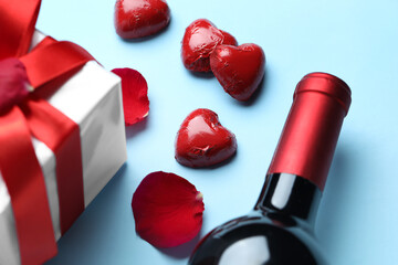 Fototapeta na wymiar Bottle of wine, candies and gift on blue background, closeup. Valentine's Day celebration