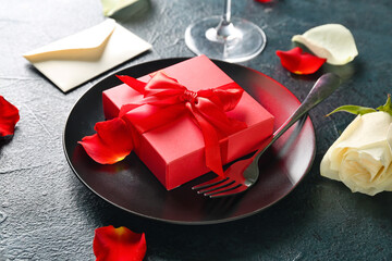 Plate with beautiful gift for Valentine's Day celebration and rose petals on dark color background