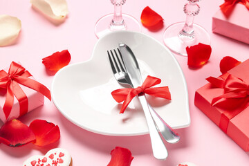 Heart shaped plate, cutlery, gifts for Valentine's Day celebration and rose petals on pink background