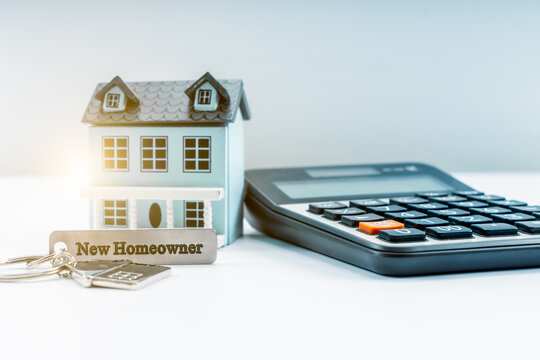Classic house model, house key with "new homeowner" and calculator on white background.