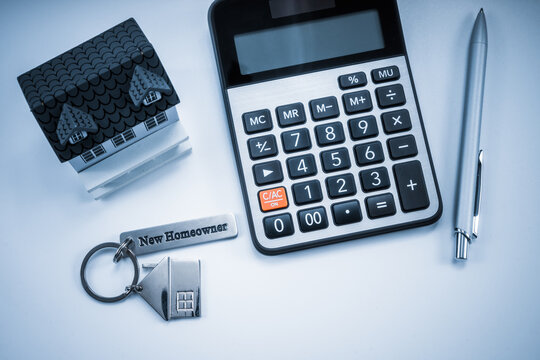 Classic house model, house key with "new homeowner", calculator and pen on white background.