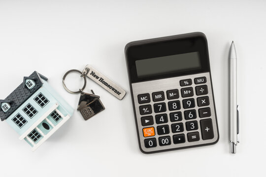 Classic house model, house key with "new homeowner", calculator and pen on white background.