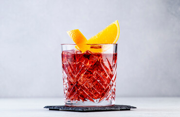 Fototapeta Negroni popular alcoholic cocktail with dry gin, red vermouth and red bitter, orange slice and ice cubes. Gray bar counter background, bar tools, copy space obraz