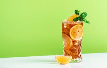 Long Island ice tea cocktail with vodka, rum, tequila, gin, liquor, lemon juice, cola and ice, garnished with lemon slice and mint in highball glass. Green background